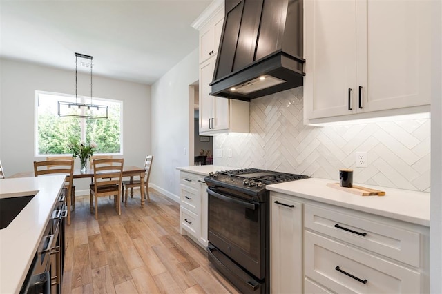 kitchen with custom exhaust hood, black gas range oven, pendant lighting, light hardwood / wood-style floors, and white cabinets