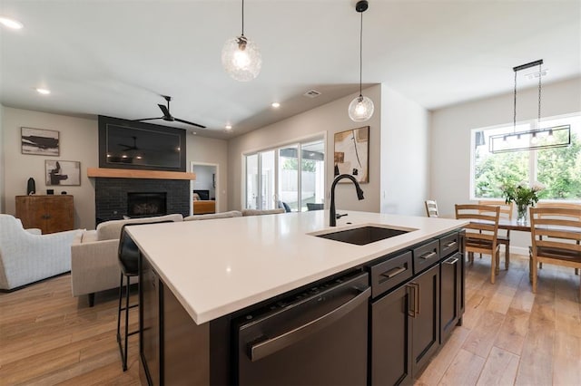 kitchen with pendant lighting, dishwasher, sink, a kitchen island with sink, and a brick fireplace