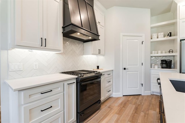 kitchen with black gas range, white cabinetry, tasteful backsplash, custom exhaust hood, and light wood-type flooring