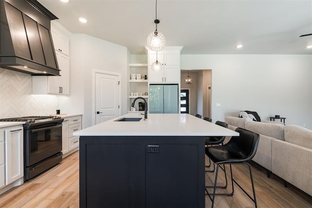 kitchen featuring premium range hood, a kitchen island with sink, white cabinets, and gas range oven