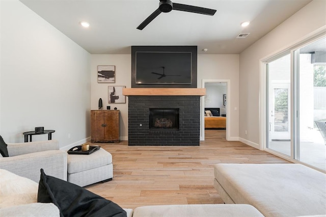 living room featuring a brick fireplace, ceiling fan, and light hardwood / wood-style flooring