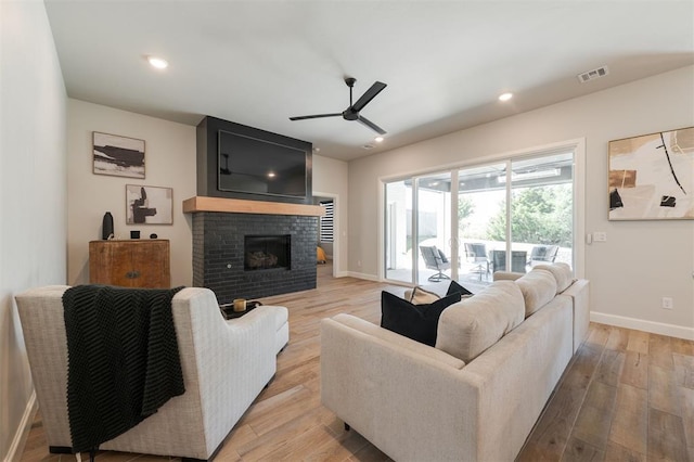 living room featuring ceiling fan, a brick fireplace, and light wood-type flooring