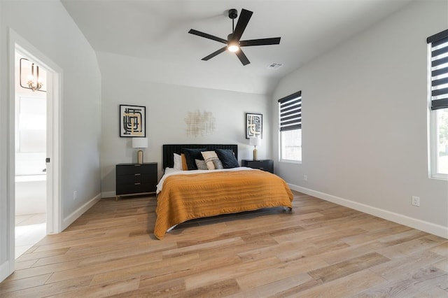 bedroom with ceiling fan with notable chandelier, vaulted ceiling, ensuite bathroom, and light wood-type flooring