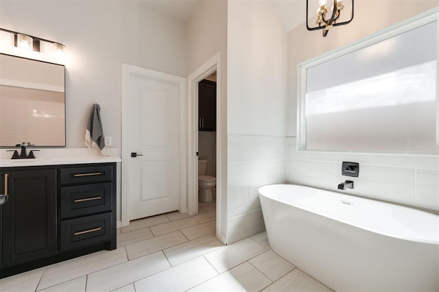 bathroom with tile walls, a bathtub, vanity, a notable chandelier, and toilet