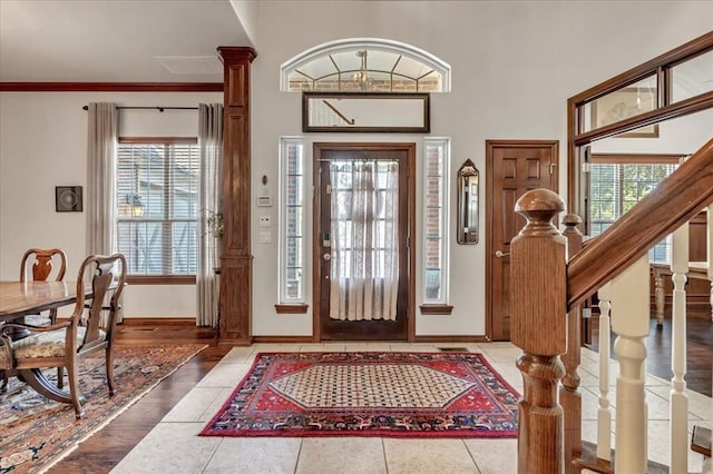 tiled foyer entrance with ornamental molding, decorative columns, and a healthy amount of sunlight