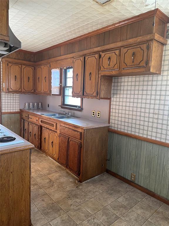 kitchen with white electric cooktop, sink, wooden walls, and wall chimney exhaust hood