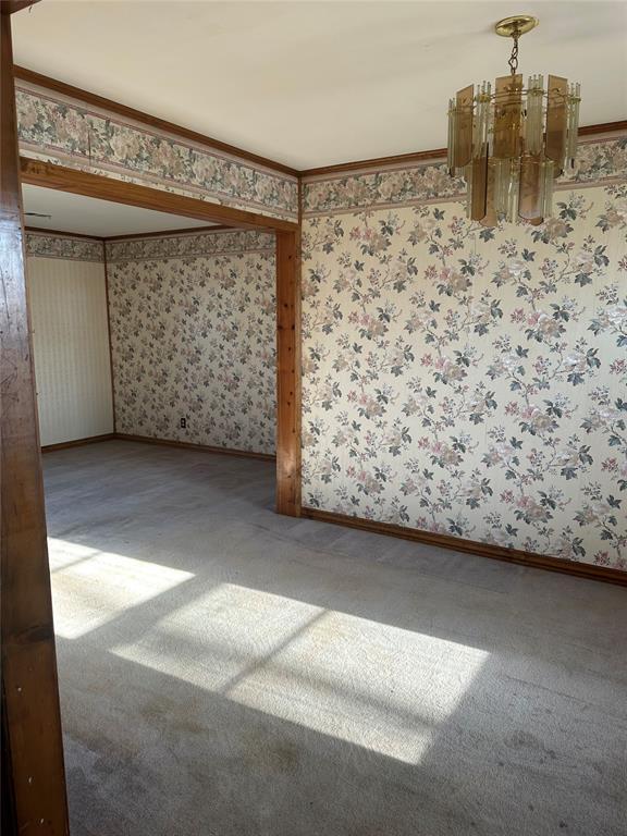 carpeted empty room with an inviting chandelier and crown molding