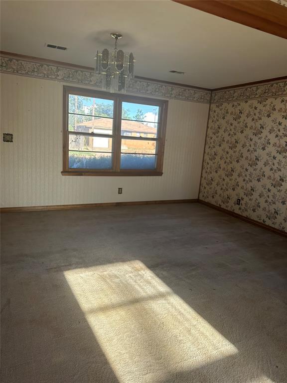 empty room featuring ornamental molding, carpet, and a chandelier