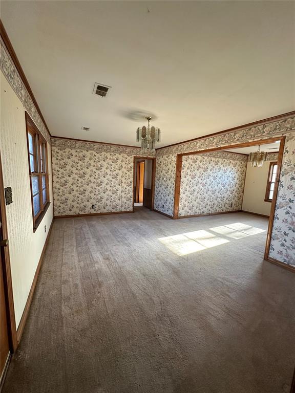 carpeted empty room featuring ornamental molding and a notable chandelier