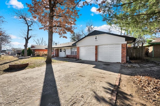 view of front facade with a garage, driveway, brick siding, and fence