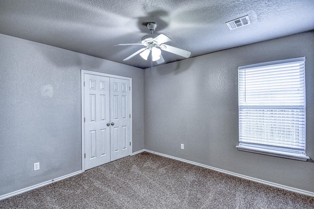 spare room featuring carpet floors, ceiling fan, baseboards, a textured ceiling, and a textured wall