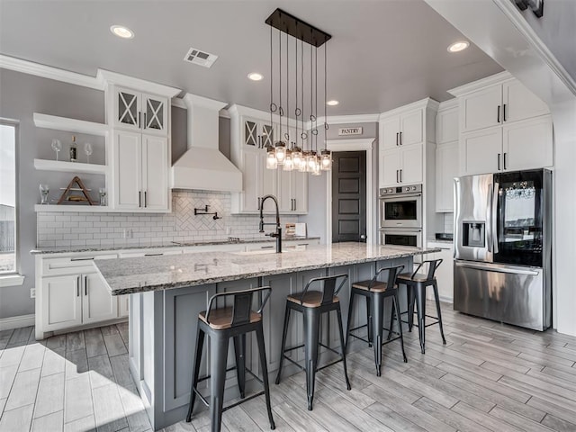 kitchen with wall chimney exhaust hood, a breakfast bar, white cabinetry, stainless steel appliances, and a kitchen island with sink