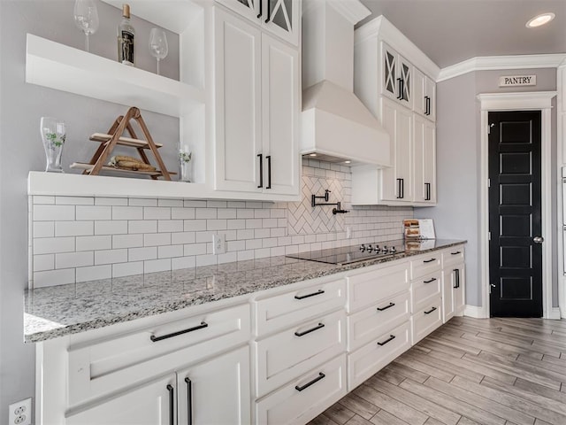 kitchen featuring crown molding, white cabinetry, light stone counters, black electric stovetop, and custom exhaust hood