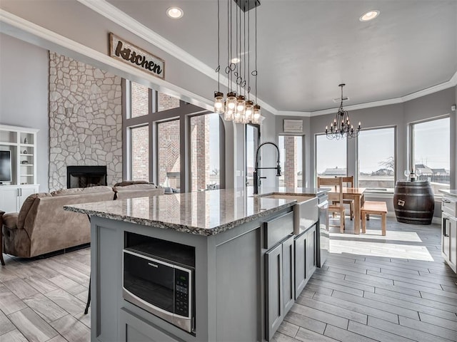 kitchen featuring pendant lighting, crown molding, a kitchen island with sink, gray cabinetry, and light stone countertops