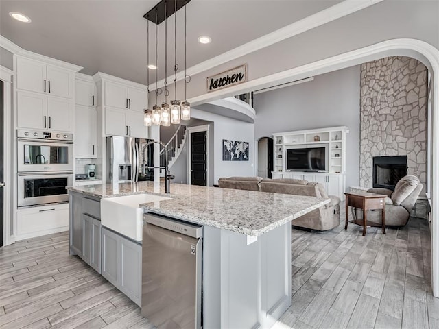 kitchen with pendant lighting, a kitchen island with sink, stainless steel appliances, white cabinets, and a stone fireplace