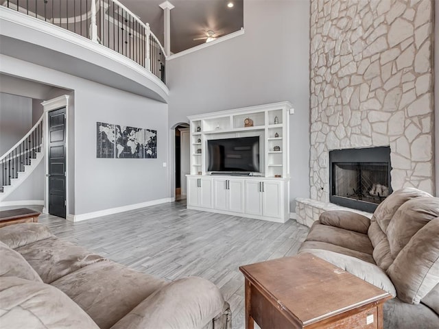 living room featuring ceiling fan, a towering ceiling, a fireplace, and light hardwood / wood-style flooring