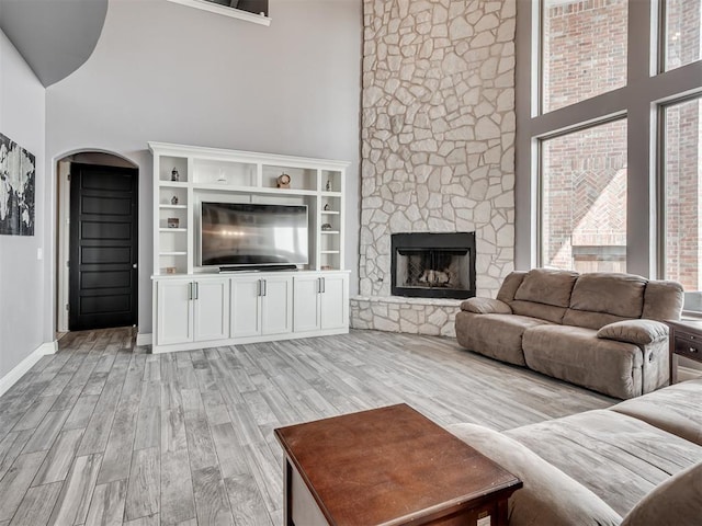 living room with a stone fireplace, light hardwood / wood-style flooring, and a high ceiling