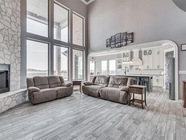 living room featuring a stone fireplace, light hardwood / wood-style flooring, a chandelier, and a high ceiling