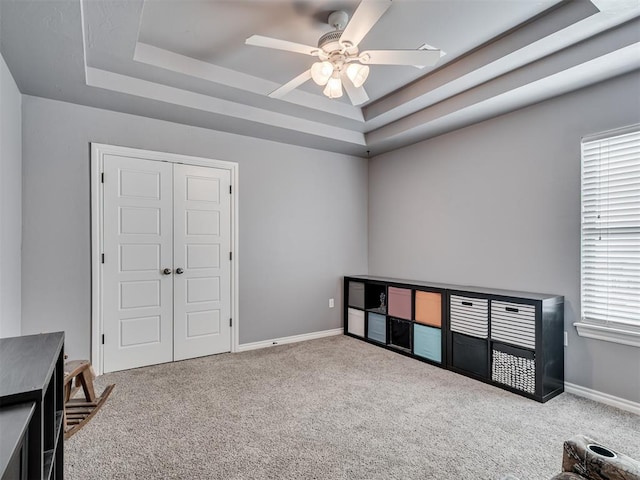 interior space with a raised ceiling, ceiling fan, and carpet flooring