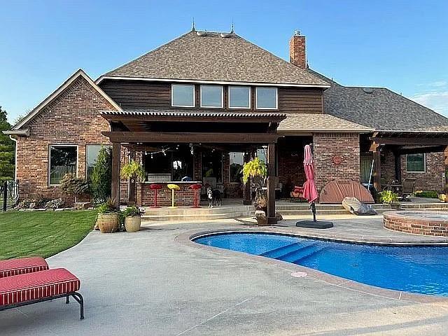 rear view of house featuring a patio and a pool with hot tub