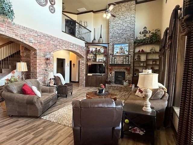 living room featuring crown molding, a stone fireplace, wood-type flooring, and a towering ceiling