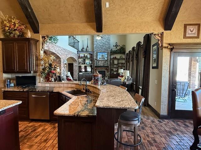 kitchen featuring beamed ceiling, a stone fireplace, a kitchen island with sink, and a kitchen bar