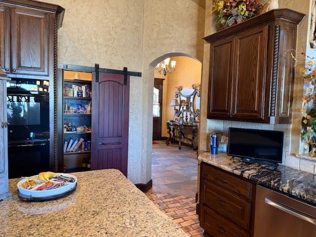 kitchen with light stone counters, backsplash, stainless steel dishwasher, a barn door, and a high ceiling