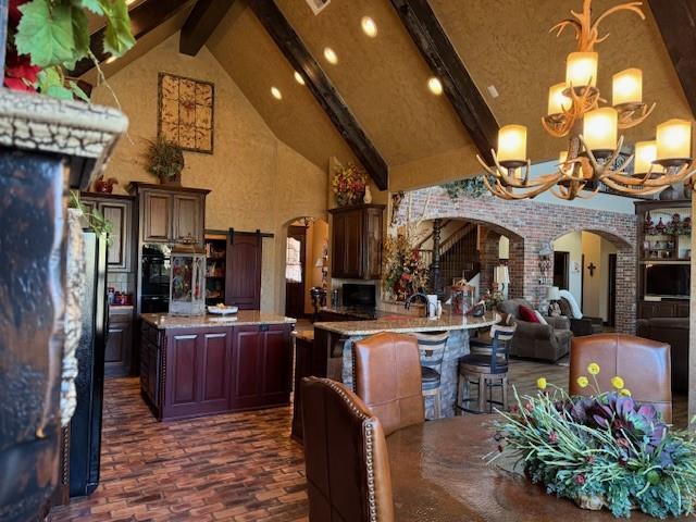 kitchen featuring an inviting chandelier, beam ceiling, high vaulted ceiling, light stone counters, and a kitchen island