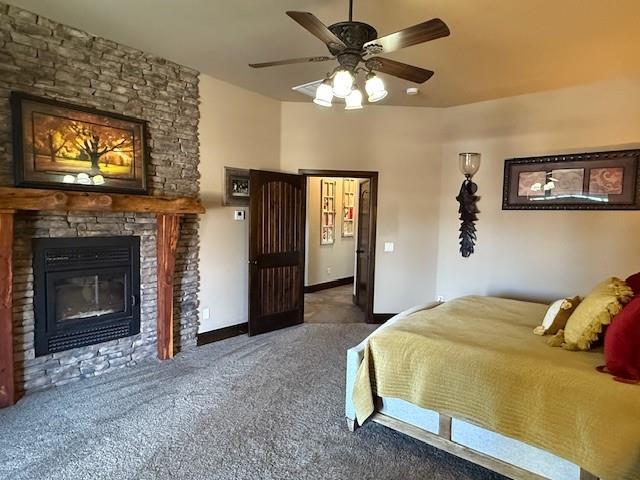 carpeted bedroom with a stone fireplace and ceiling fan