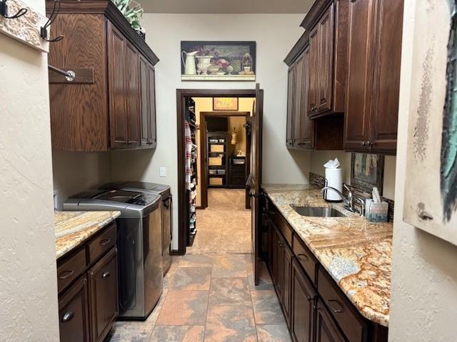 kitchen with light stone counters, dark brown cabinetry, sink, and washer and dryer