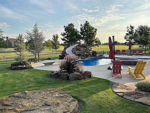 view of pool featuring a water slide, a yard, a patio, and an in ground hot tub