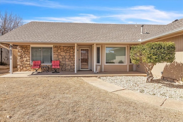 rear view of house with stone siding, a shingled roof, and fence