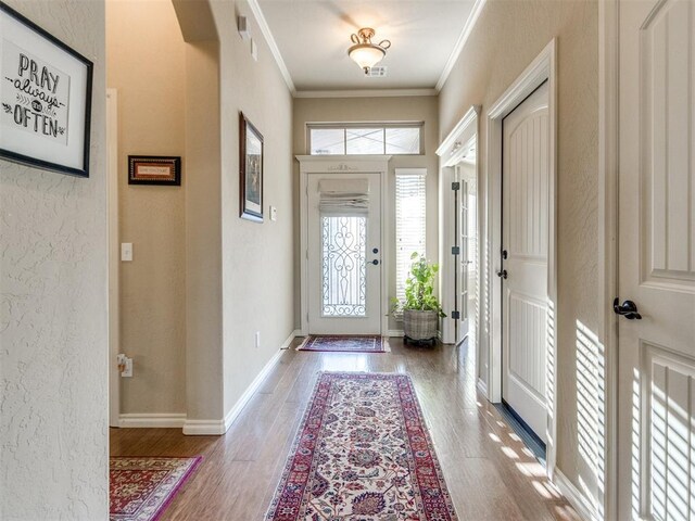 entrance foyer with baseboards, crown molding, wood finished floors, and a textured wall