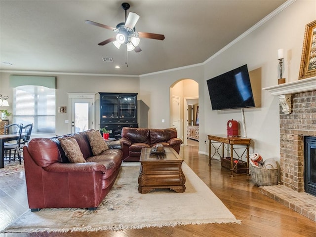 living room with visible vents, a brick fireplace, ceiling fan, wood finished floors, and arched walkways