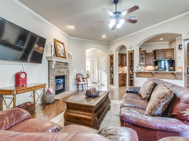 living room featuring a brick fireplace, visible vents, light wood-type flooring, and a ceiling fan
