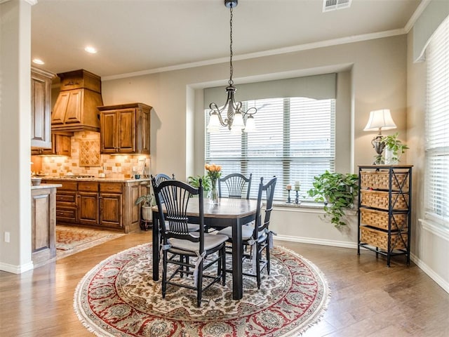dining area with light wood finished floors, baseboards, a notable chandelier, and crown molding