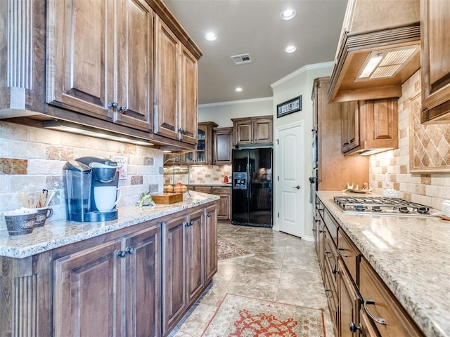 kitchen featuring crown molding, black refrigerator with ice dispenser, stainless steel gas stovetop, visible vents, and extractor fan