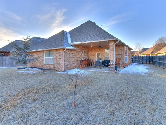 rear view of house with roof with shingles, a fenced backyard, ceiling fan, brick siding, and a patio area