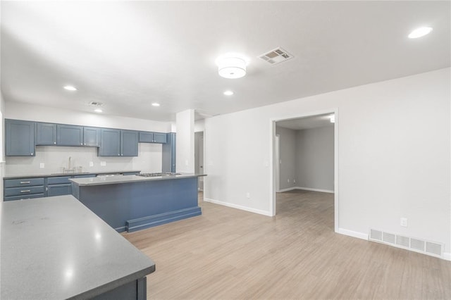 kitchen with sink, stainless steel gas cooktop, a kitchen island, decorative backsplash, and light wood-type flooring