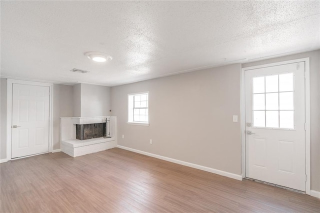 unfurnished living room featuring a textured ceiling, a brick fireplace, and light hardwood / wood-style flooring