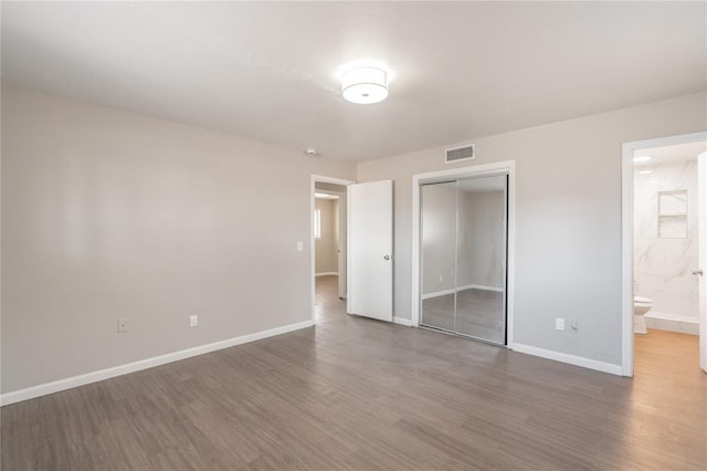 unfurnished bedroom featuring ensuite bath, dark hardwood / wood-style flooring, and a closet