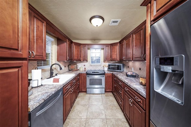 kitchen featuring sink, appliances with stainless steel finishes, backsplash, light stone countertops, and light tile patterned flooring