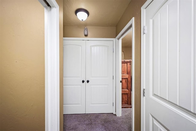 corridor with a textured ceiling and dark carpet