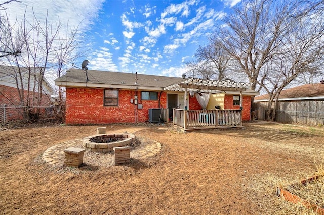 rear view of house with a fenced backyard, a fire pit, central AC, and brick siding