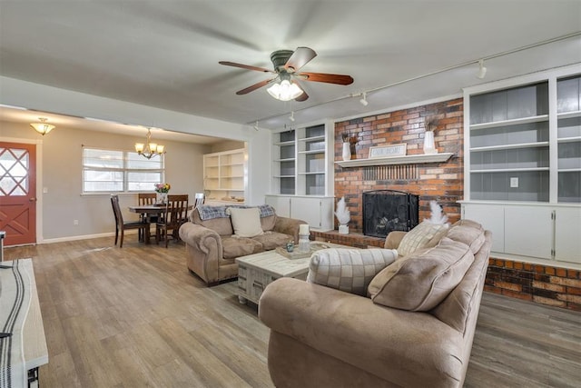 living room featuring built in shelves, rail lighting, a brick fireplace, hardwood / wood-style floors, and ceiling fan with notable chandelier