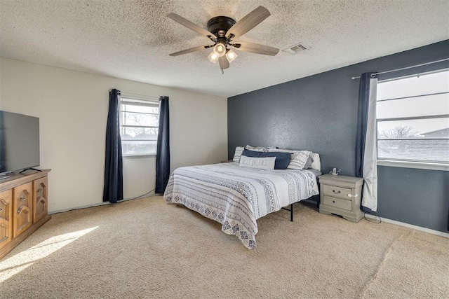 bedroom with a textured ceiling, light colored carpet, and ceiling fan