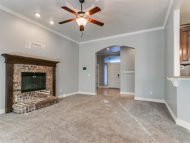 unfurnished living room with a brick fireplace, ornamental molding, ceiling fan, and carpet