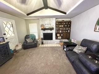 carpeted living area with a brick fireplace and vaulted ceiling with beams