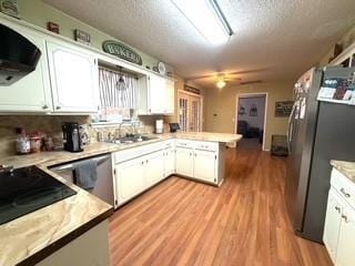 kitchen featuring ventilation hood, a peninsula, stainless steel appliances, light countertops, and white cabinetry