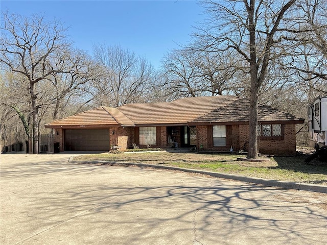 view of front of home with a tiled roof, an attached garage, brick siding, and driveway
